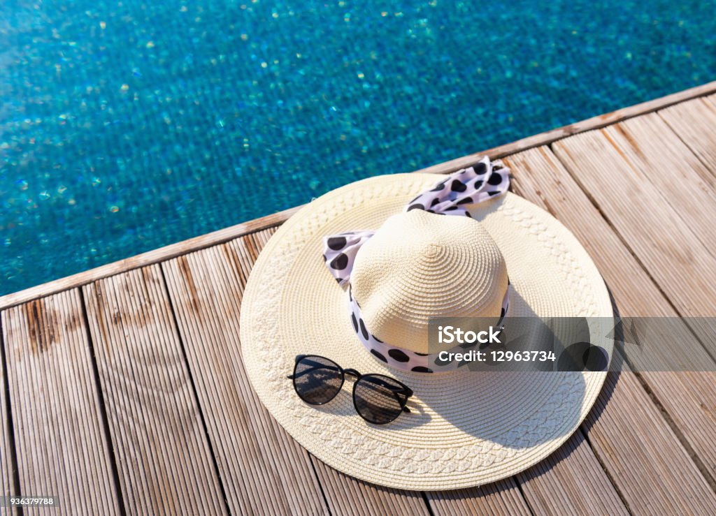 Straw sun hat and sunglasses on the terrace of swimming pool Straw sun hat and sunglasses on the terrace of swimming pool. Swimming Pool Stock Photo