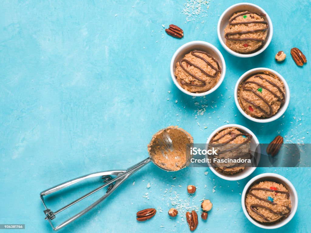 eatable raw monster cookie dough Safe-to-eat raw monster cookie dough in small portion bowl, ice cream scoop and nuts on blue background. Ideas and recipes for kids and toddlers meal. Top view or flat-lay. Copy space for text. Ice Cream Stock Photo