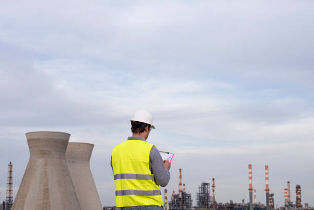 Back view of a manual worker in oil refinery industry. The worker writing report, using clipboard.