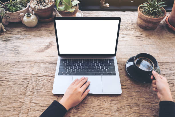 istock Top view mockup image of hands using and typing on laptop with blank white desktop screen and holding coffee cup on vintage wooden table in cafe 936382954