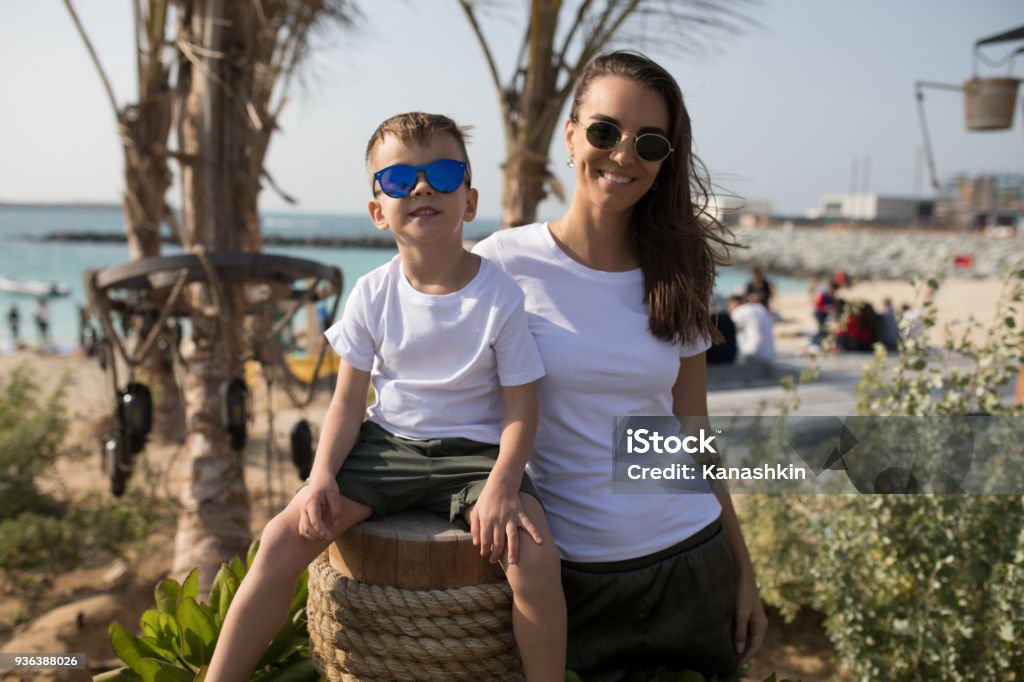Woman with her son in white T-shirts standing on the beach. Adult Stock Photo