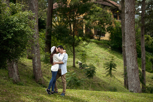 Young Asian couple hugging in nature, woman kissing her boyfriend on forehead