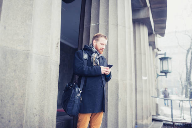 istock Ginger businessman standing on office building entrance, using mobile phone 936397406