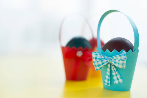 Colorful eastern eggs warped in paper cups on yellow background. Selective focus