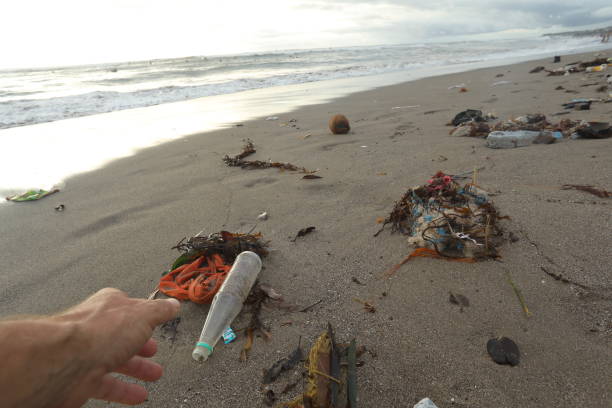 istock Hand reaches for plastic bottle and garbage on beach. 936398400