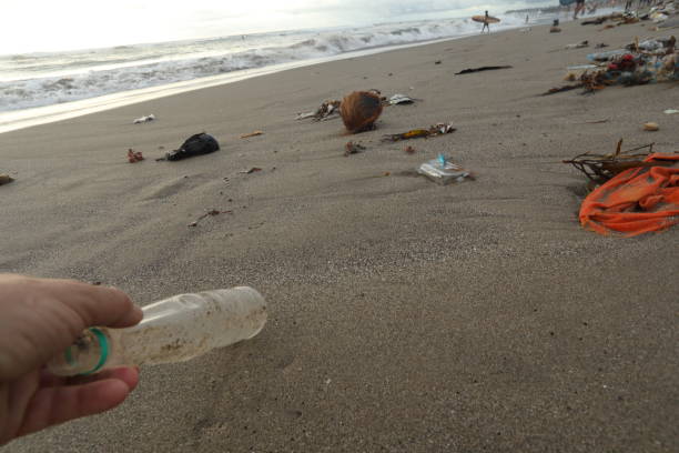 istock Hand reaches for plastic bottle and garbage on beach. 936398430
