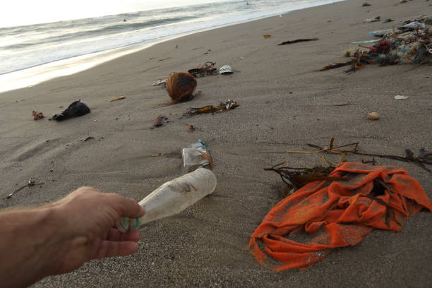 istock Hand reaches for plastic bottle and garbage on beach. 936398450
