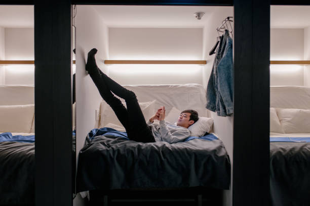 istock Young adult male lying down using a smartphone in a capsule hotel 936399612
