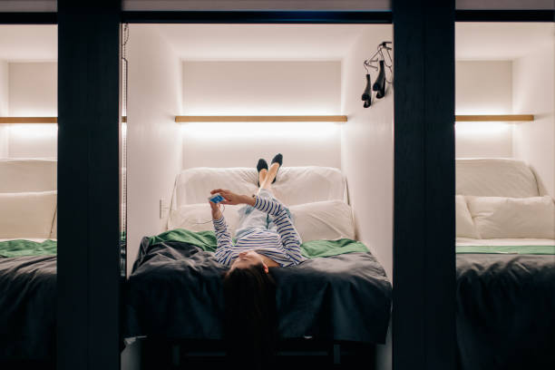 Young woman lying on a bed using a smartphone in a capsule hotel. Tokyo, Japan. March 2018