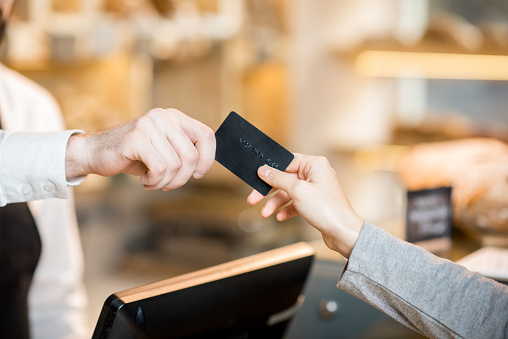 Paying by credit card in the store with bakery products. Close-up view on the hands and card
