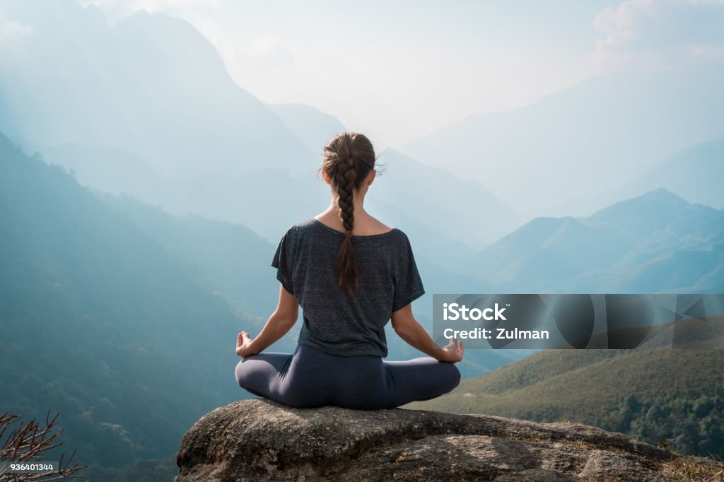 Woman meditates in yoga asana Padmasana Woman meditates in yoga asana Padmasana - Lotus pose on mountain cliff Meditating Stock Photo