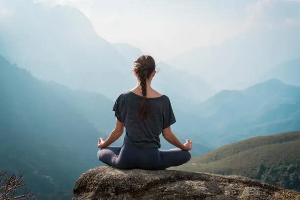 Woman meditates in yoga asana Padmasana - Lotus pose on mountain cliff