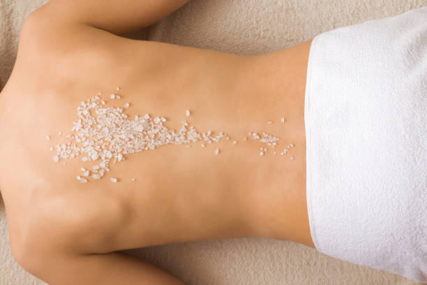 beautiful young woman lying and getting white sea salt scrub treatment in health spa. doing massage on woman's back in beauty salon. enjoying life. relaxing day. body care concept. - exfoliating scrub imagens e fotografias de stock