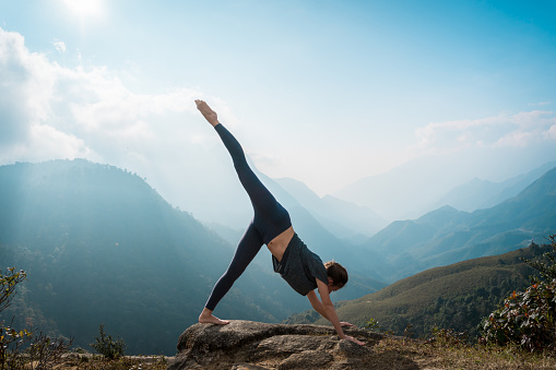 Sporty woman practicing yoga on mountain cliff at sunrise. Healthy lifestyle. Mountanious landscape