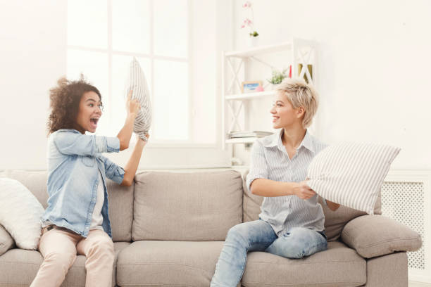 istock Two young women having pillow fight on sofa 936405028