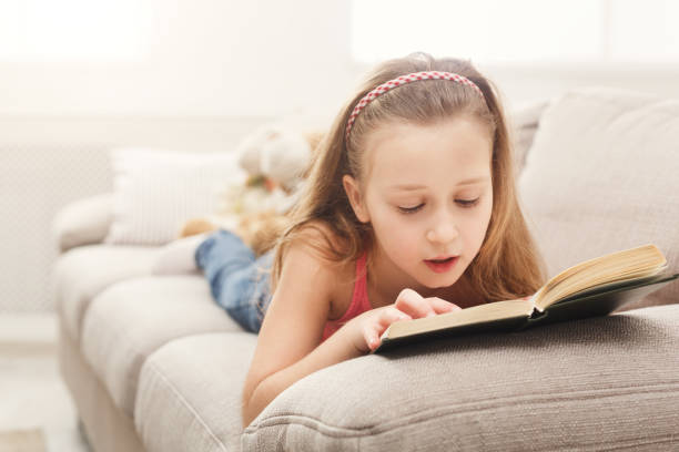 istock Pretty feamle kid reading book, lying on sofa at home 936414718
