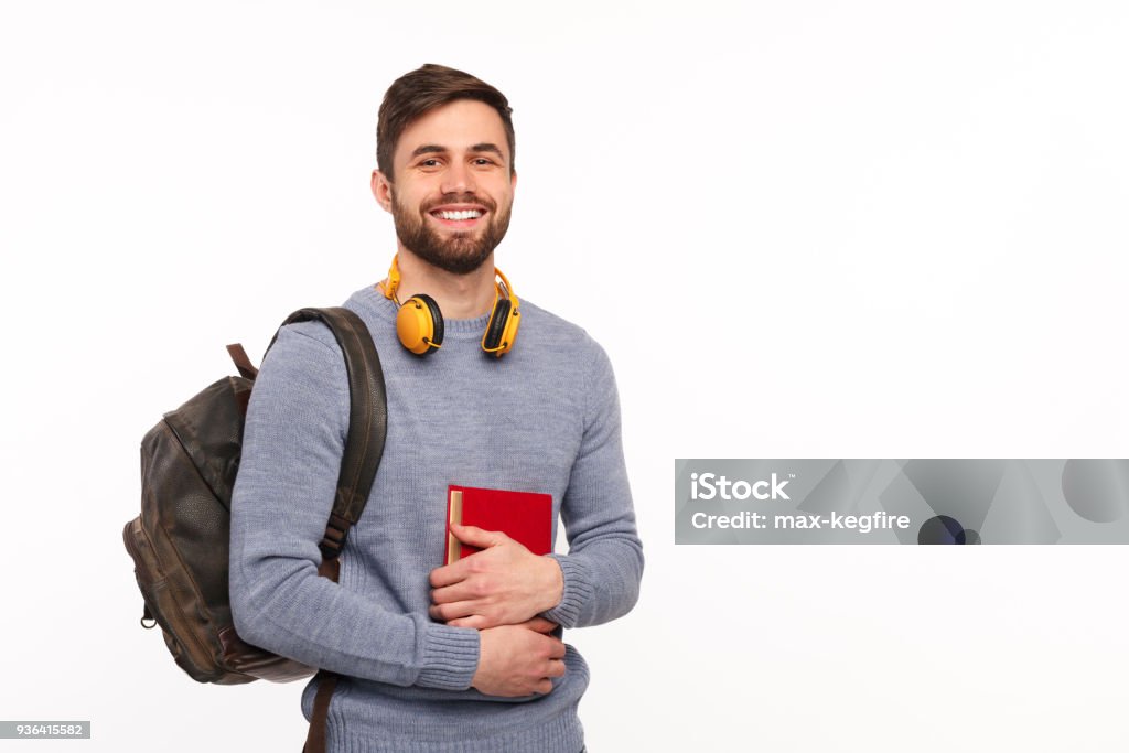 Cheerful male student with backpack Young handsome man with backpack and headphones holding book and smiling at camera. Student Stock Photo
