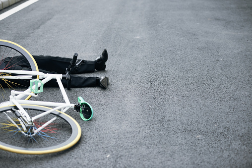 Legs of man in suit lying down near his bicycle after road accident