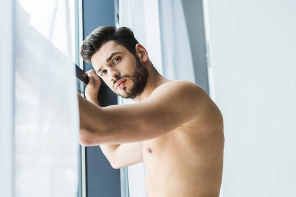 istock shirtless man standing at window and looking at camera 936416142