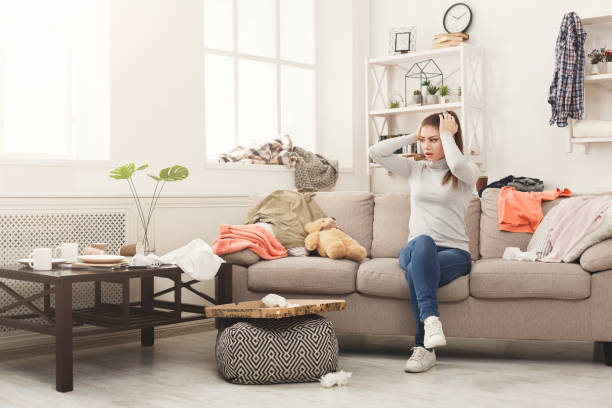 Desperate woman sitting on sofa in messy room Desperate helpless woman sitting on sofa in messy living room. Young girl surrounded by many stack of clothes. Disorder and mess at home, copy space messy stock pictures, royalty-free photos & images