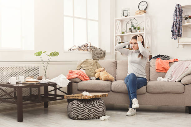 desperate woman sitting on sofa in messy room - frustration emotional stress surprise women imagens e fotografias de stock