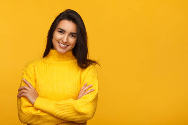Charming female on yellow backdrop Young beautiful brunette in yellow sweater standing with hands crossed on yellow. moldova stock pictures, royalty-free photos & images