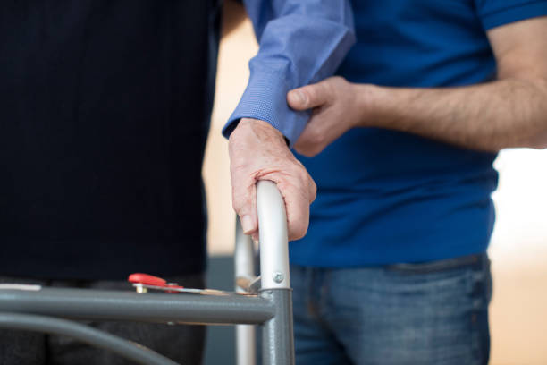 senior man's hands on walking frame z pracownikiem opieki w tle - nursing home senior adult home caregiver physical therapy zdjęcia i obrazy z banku zdjęć