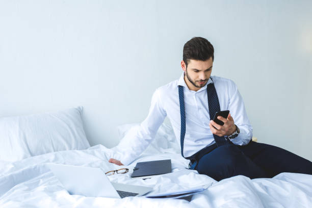 istock businessman working with smartphone, documents and laptop on bed in morning 936420444