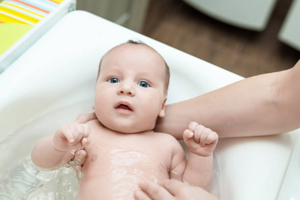 istock Cute adorable infant boy having first bath. Mother washes baby with comfortable temperature water. Newborn hygiene and healthcare concept 936425034