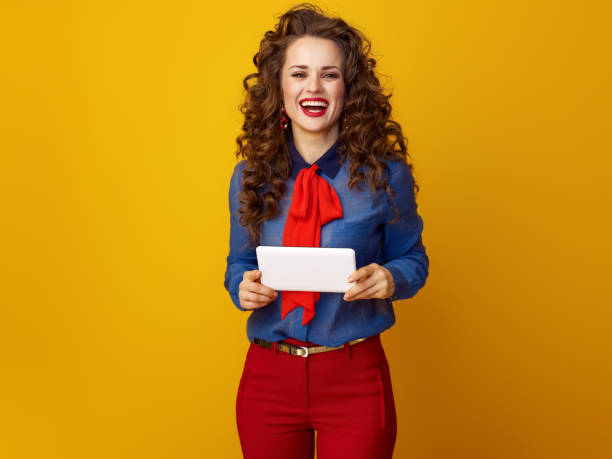 istock happy trendy woman against yellow background with tablet PC 936427188