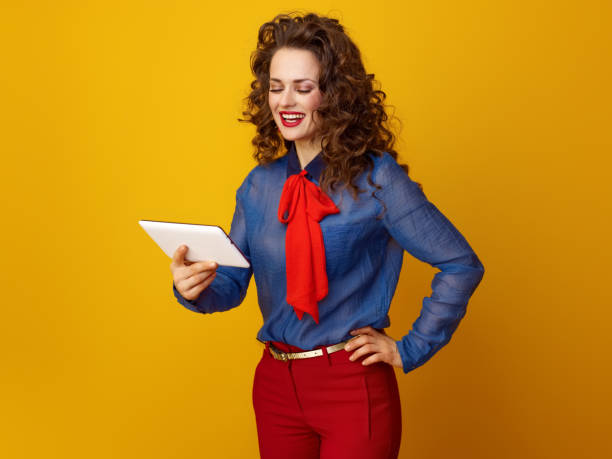 istock happy stylish woman against yellow background using tablet PC 936427260