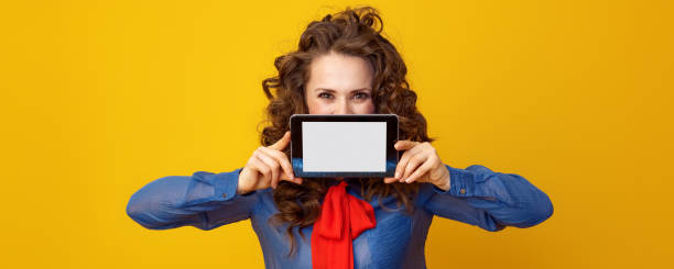 donna su sfondo giallo nascosto dietro tablet pc schermo vuoto - hiding internet multimedia people foto e immagini stock