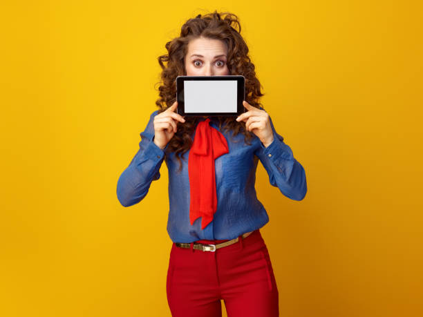 donna su sfondo giallo nascosto dietro tablet pc schermo vuoto - hiding internet multimedia people foto e immagini stock