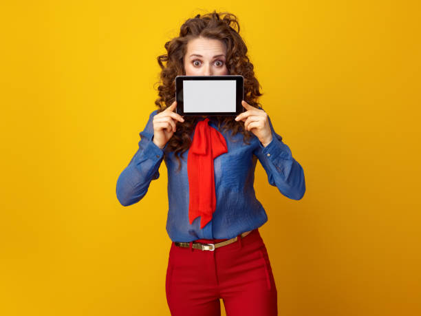 istock woman on yellow background hiding behind tablet PC blank screen 936427398