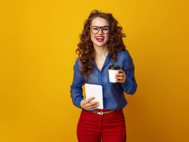 istock woman against yellow background with coffee cup and tablet PC 936428312