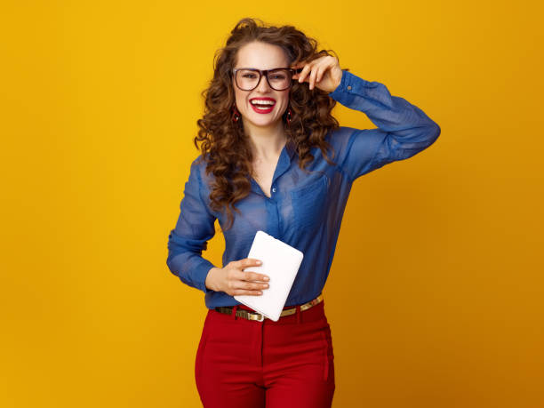 istock happy trendy woman against yellow background with tablet PC 936428354