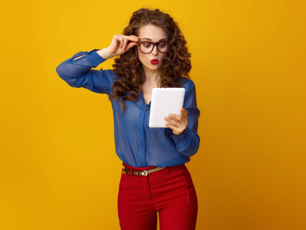 istock surprised stylish woman isolated on yellow with tablet PC 936428376