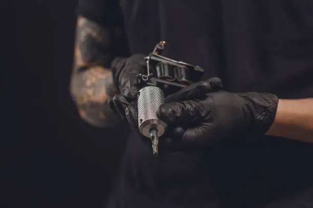 Male hands in gloves holding tattoo machine isolated on black