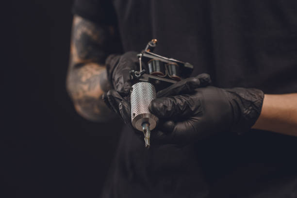 male hands in gloves holding tattoo machine isolated on black - tatuagem imagens e fotografias de stock