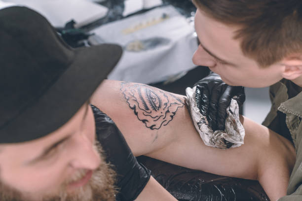 istock Master in gloves working on shoulder tattoo in studio 936429600