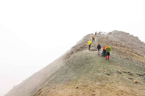 Large group of people walking in line on the edge of rocky mountain pass in the fog, close to the Alakol lake, on 3.900 m.