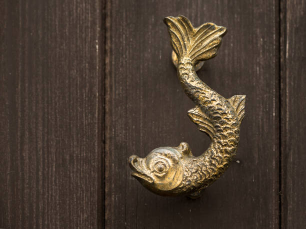 Shiny door handle made of bronze shape of a fish on a wooden garden door