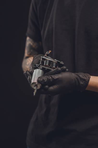 istock Tattoo machine in male hands isolated on black 936432880