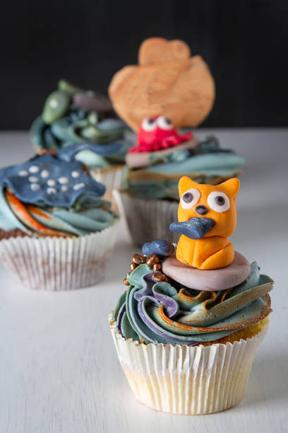 istock Capcake with animals from mastic and marzipan cat, fish and crab. Decor cake. Dark background. 936434082