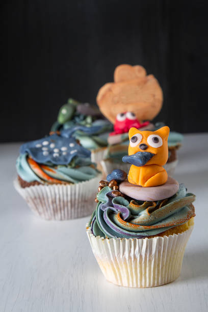 istock Capcake with animals from mastic and marzipan cat, fish and crab. Decor cake. Dark background. 936434278