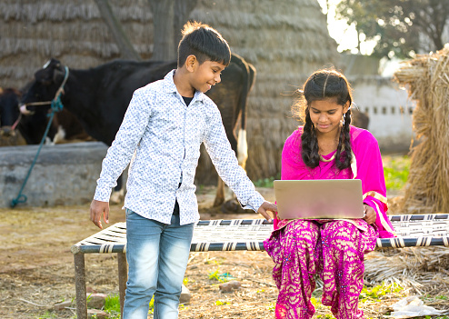 Brother and sister using laptop on traditional bed in village