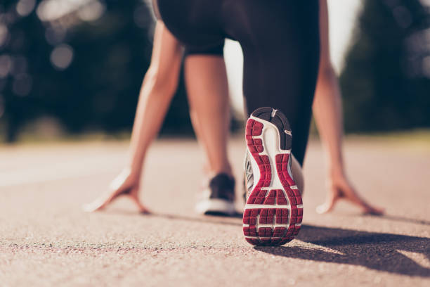 prêt à partir ! gros plan photo recadrée faible angle de chaussure de l’athlète féminine sur la ligne de départ d’une piste de stade, préparation pour une course. journée de printemps ensoleillée - athlete running sport jogging photos et images de collection