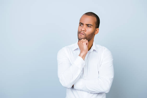 Skeptic, unsure, uncertain, doubts concept. Young african guy in formal wear is looking sceptical, has a grimace of distrust on light blue background