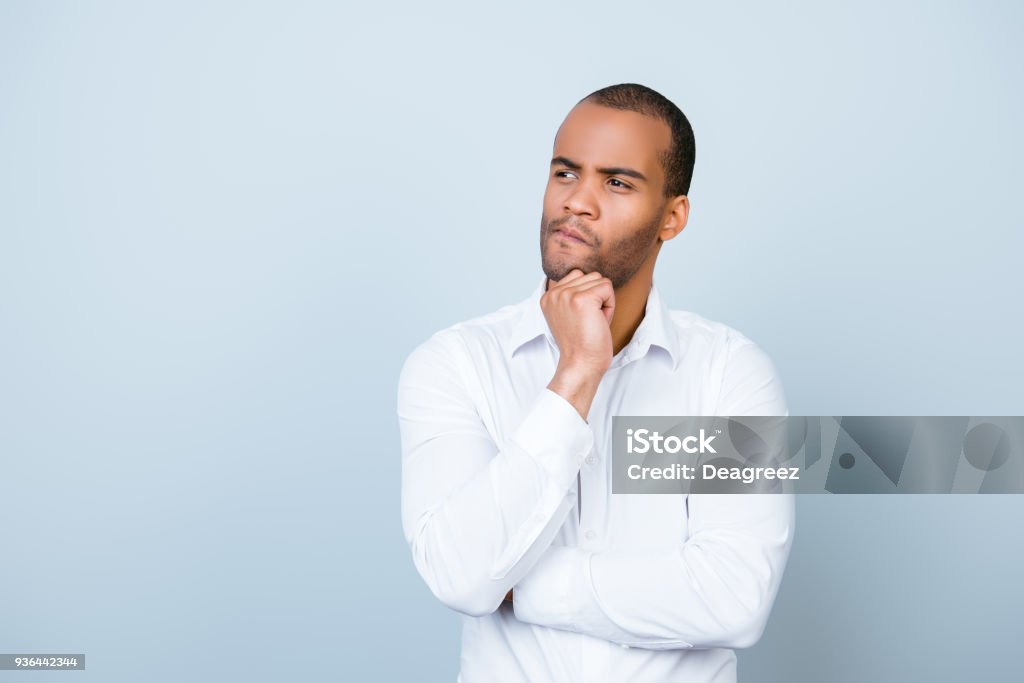 Skeptic, unsure, uncertain, doubts concept. Young african guy in formal wear is looking sceptical, has a grimace of distrust on light blue background Contemplation Stock Photo