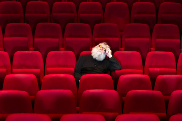 istock One man with white beard sits in Empty cinema or theatre with comfortable red seats, sleeping 936452824